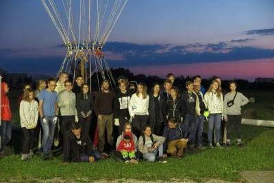 Gruppenbild auf dem Gasballonstartplatz in der Morgendämmerung. Die Gruppe hat sich vor dem Korb des gefüllten Gasballons positioniert.