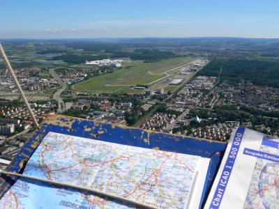 Der Kontakt zur Flugsicherung, am Flughafen oder auf Strecke gehört zu den Aufgaben des Piloten. Im Bild im Vordergrund das Kartenbrett des Ballons, mit Straßen- und Luftfahrerkarte, und im Hintergrund der Flughafen Friedrichshafen.